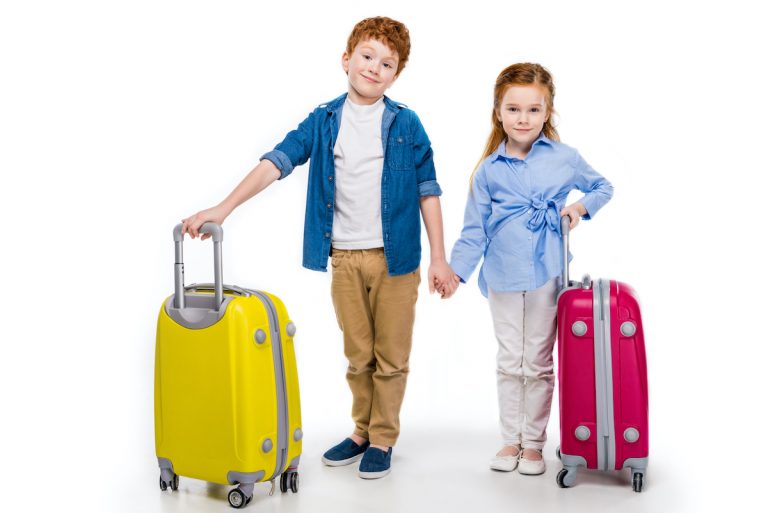 Young brother and sister holding hands while standing with suitcases