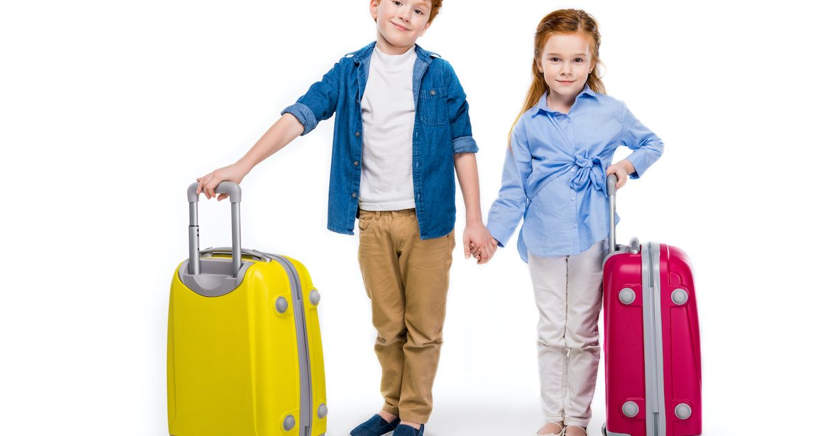 Young brother and sister holding hands while standing with suitcases